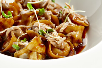 Main course in italian cuisine - meat tortellini with demi-glace sauce and mushroom cream. Beef ravioli on white plate. Tortellini with minced veal in beef sauce. Gourmet cuisine in restaurant menu.