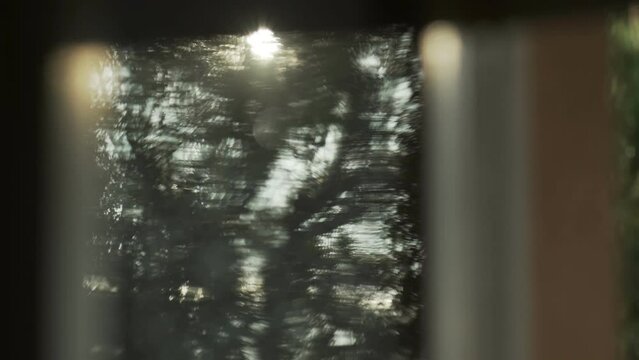 Beautiful abstract reflections on wet glass after rain. Solar glare on the window. Drops of water and blurry reflections of trees in the window. Shiny bokeh spots. Video background.