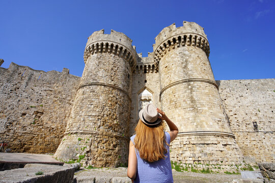 Tourism in Greece. Back view of tourist girl walking down the Marine Gate main entrance to Rhodes town from the harbour, Greece. Unesco world heritage site.