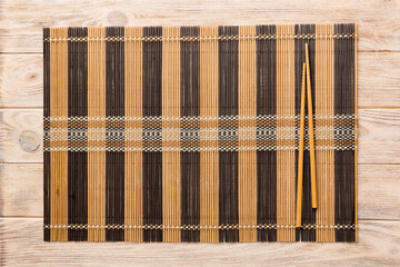 Two chopsticks and bamboo mat on wooden background. Top view, copy space