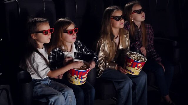 In 3D glasses. Four kids sitting in the cinema and eating popcorn