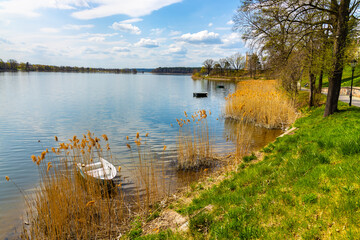Panoramic spring view of Jezioro Elckie lake with reed and wooded shoreline along touristic promenade in Elk town of Masuria region of Poland