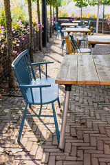 Tables and chairs on a charming empty terrace of a restautant, sunny and surrounded by flowers