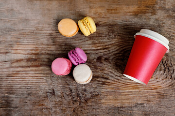 Fototapeta na wymiar red paper cup with coffee and macaroons on a wooden background. Coffee to go with cakes with copy space