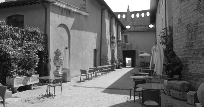Black and white shot of outdoors of kichen museum next to circo roma with chairs and tables lined in a row by the side of a gravel path in Rome, Italy. 4K