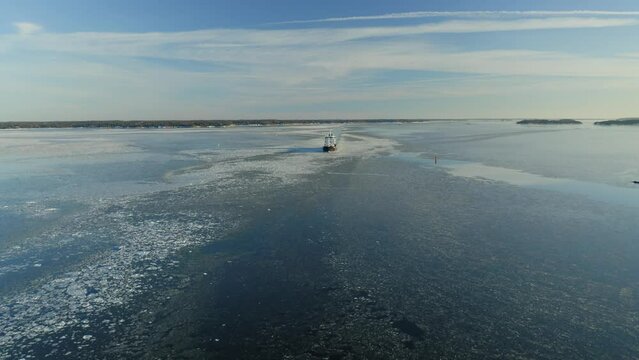 Oil and Chemical tanker making way ahead in narrow fairway in beautiful Finnish archipelago during winter evening. Light clouds, glassy sea surface with light ice floes. Aerial front view.