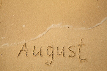 August - drawing handwritten on the sea beach sand.