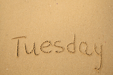 Tuesday - drawing of days of the week, handwritten on the sea beach sand.
