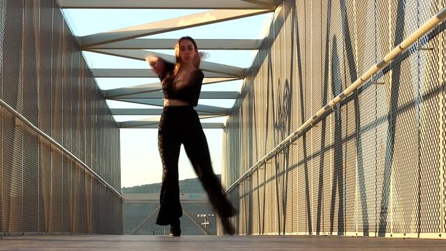 vertical portrait of a young caucasian woman dancing urban dance at sunset on a bridge. waacking dance style