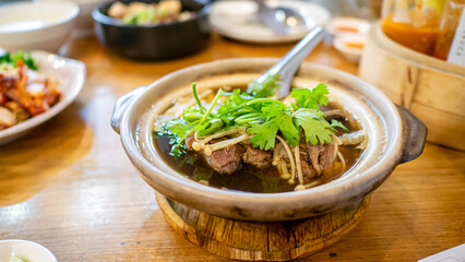 Bak Kut Teh, a close up of Chinese pork rib soup in traditional bowl pot on wooden table at Thai restaurant in Bangkok, Thailand.