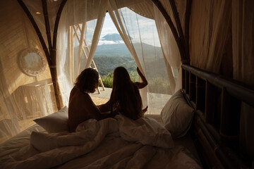 Сouple in love on a bed with a beautiful view of the mountains from a bamboo house. Bamboo house with mountain or volcano view in Bali.