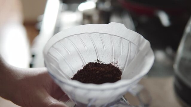 Barista pouring ground beans from a grinder into a paper filter, v60. funnel 