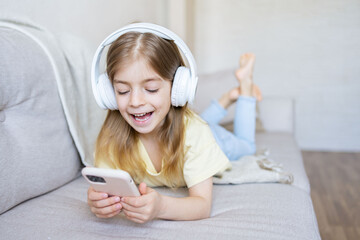 Beautiful smiling little girl with headphones using a smartphone at home.home, leisure, new technology and music concept.
