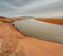 The shore of the Krasnoyarsk reservoir without water, sandy ripples, clay and hills, rainy sky over Mount Tepsey Tepsei