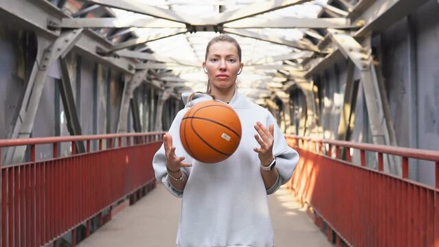 Young sporty woman with wireless headphones hold basketball ball on urban background. Concept of active lifestyle
