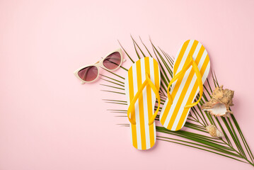 Summer rest concept. Top view photo of yellow striped flip-flops trendy sunglasses shells and palm leaves on isolated pastel pink background