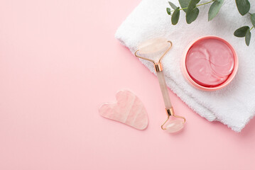 Beauty procedure concept. Top view photo of rose quartz roller pink eye patches gua sha white cotton towel and eucalyptus on pastel pink background with copyspace