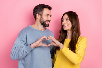 Portrait of attractive cheerful amorous couple showing heart symbol amour isolated over pink pastel...
