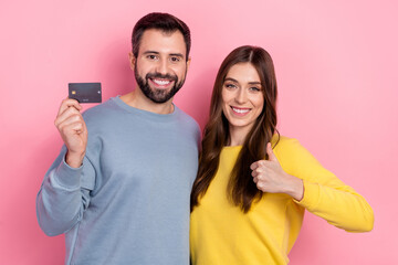 Portrait of beautiful handsome cheery friends friendship showing thumbup bank card isolated over pink pastel color background
