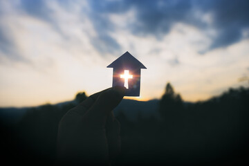 Hand holding home cross shapes. with light of sunset background,  christian silhouette concept. - obrazy, fototapety, plakaty