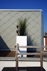 Dachterrasse der Ferienwohnung mit grauer Fassadenverkleidung und Grünpflanze in weißem Behälter vor blauem Himmel im Sonnenschein in Knokke-Heist an der Nordsee bei Brügge in Westflandern in Belgien