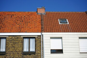 Wohnhäuser mit Gardine und Rollos als Sonnenschutz und rotbraunen Ziegeldächern vor blauem Himmel...