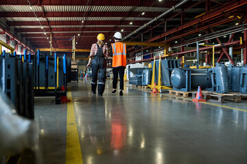 Rear view of two young female engineers in workwear moving along wide aisle in large workshop of...