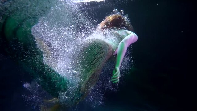 a mermaid swims away into the dark abyss in streams of bubbles. view from the back. the middle plan