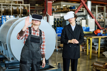 Two young engineers in vr goggles discussing characteristics of 3d product while standing in...