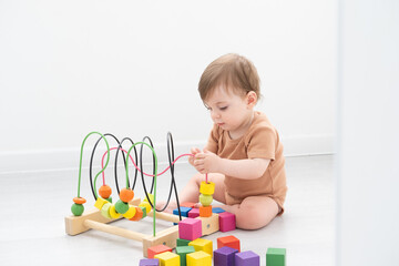 cute baby girl in brown bodysuit playing with colorful wooden toys on white room