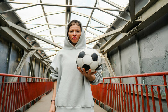 Young sporty woman football player wearing hoodie hold soccer ball on urban background.