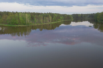 Zbiornik wodny, zalew położony w lesie. Brzegi porośnięte drzewami. Niebo jest lekko zachmurzone. Zdjęcie z drona.