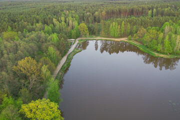 Zbiornik wodny, zalew położony w lesie. Brzegi porośnięte drzewami. Widoczna jest mała elektrownia wodna. Zdjęcie z drona.