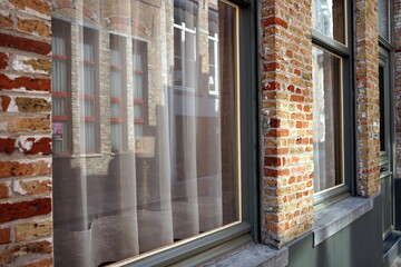 Gardinen als Sichtschutz hinter spiegelnden Fensterscheiben in schönem alten Mauerwerk aus Backstein im Sonnenschein in den Gassen der Altstadt von Brügge in Westflandern in Belgien