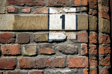 Aufgemalte Hausnummer 1 auf altem rotbraunem Backstein einer Fassade bei Sonnenschein in den Gassen...