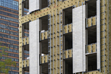 Installation of external wall thermal insulation with rock wool. Monolithic concrete frame of apartment building under construction with partially attached facade cladding blocks. Energy efficiency