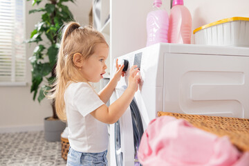 Curious cute little girl 3 year old toddler baby playing and turning on the washing machine,...