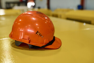 Protective helmet of orange color on yellow metallic cover of industrial machine or other equipment inside workshop of modern factory