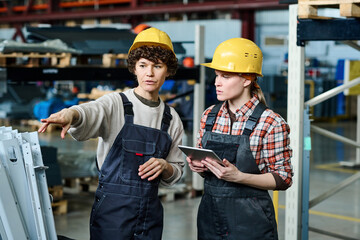 Confident female engineer pointing at industrial equipment during discussion or explanation of how it works to colleague with tablet