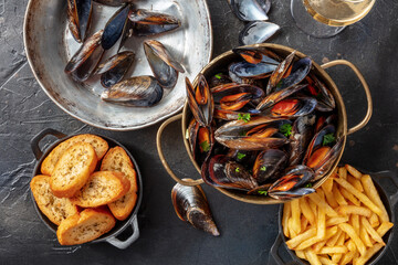 Cooked mussels with French fries and toasted bread, with wine, shot from the top on a black stone background - obrazy, fototapety, plakaty