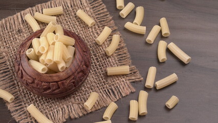 Raw penne pasta in bowl on wooden background.