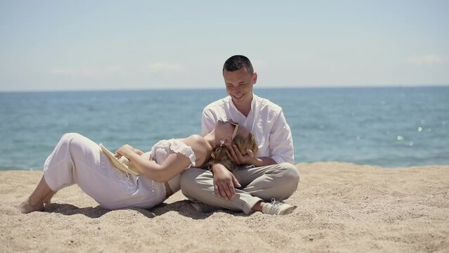 The couple is relaxing on the beach. A girl with a guy lies on the background of the ocean in white clothes, relaxes, summer vacation.