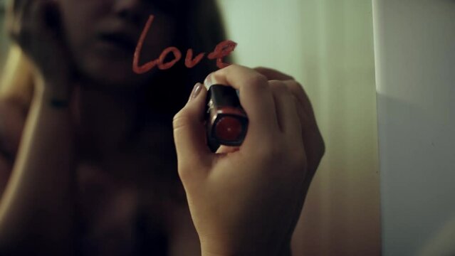 The girl writes a note on the mirror with red lipstick, love you