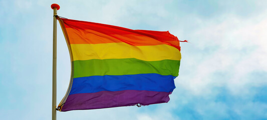 LGBT background - Rainbow flag waving on blue sky with clouds