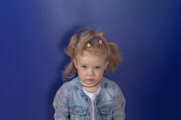 Blonde caucasian girl with funny ponytails on her head in a denim jacket on a blue background