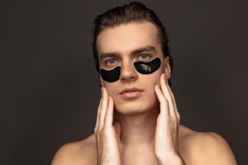 Fototapeta Young adorable man with well-kept skin using patches under eyes isolated over grey background. Fashion, cosmetics, health care, skin care, beauty obraz