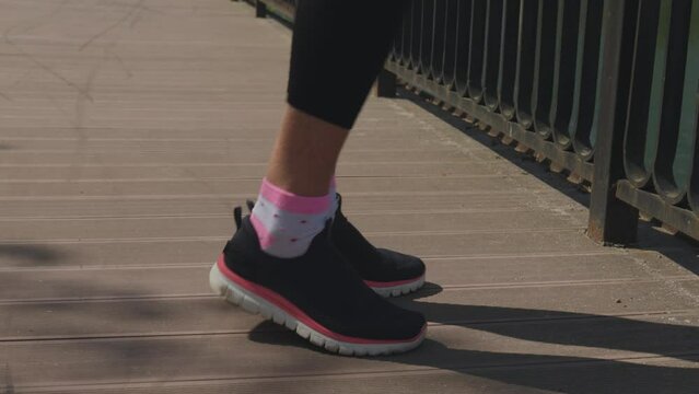 legs in black pink snickers warming up on wooden path in park, feet rotation exercises, close-up. concept of healthy lifestyle, sport outdoors, working out fresh air, steps nft finances, money concept