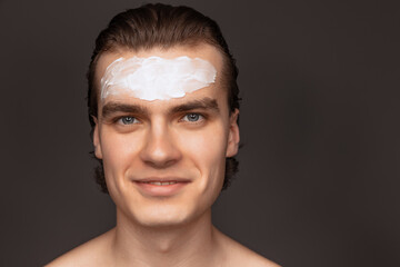 Moisturizing face mask. One man with perfect well-kept skin using face cream mask isolated over grey background. Cosmetics, health care, skin care, beauty