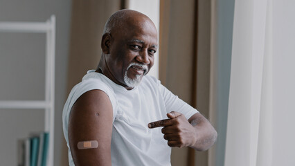 Portrait african american old senior mature man patient shows medical plaster on shoulder injection mark satisfied male after vaccination with covid-19 virus vaccine antivirus dose healthcare concept - obrazy, fototapety, plakaty