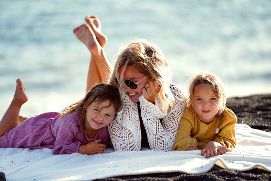 Happy woman relaxing with her two daughters outdoor on the beach, lying, talking and smiling. Mother's day. Children's day.